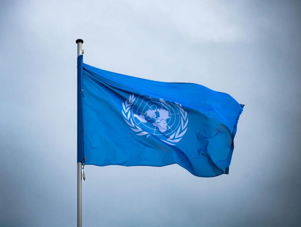 A vibrant United Nations flag on a pole waving against a muted gray sky, symbolizing global unity.